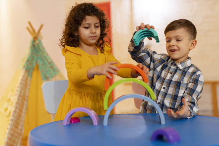 Young boy and girl playing with colorful rainbow stacking arches at a preschool activity table, promoting hands-on learning and creativity in a vibrant classroom setting