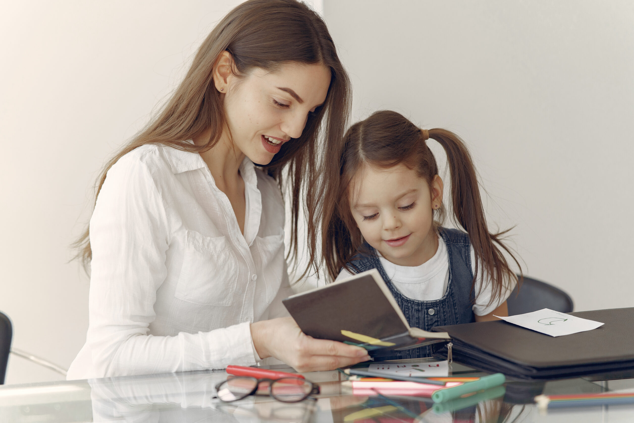 Mother helping a young girl study at home with books and stationery on the table